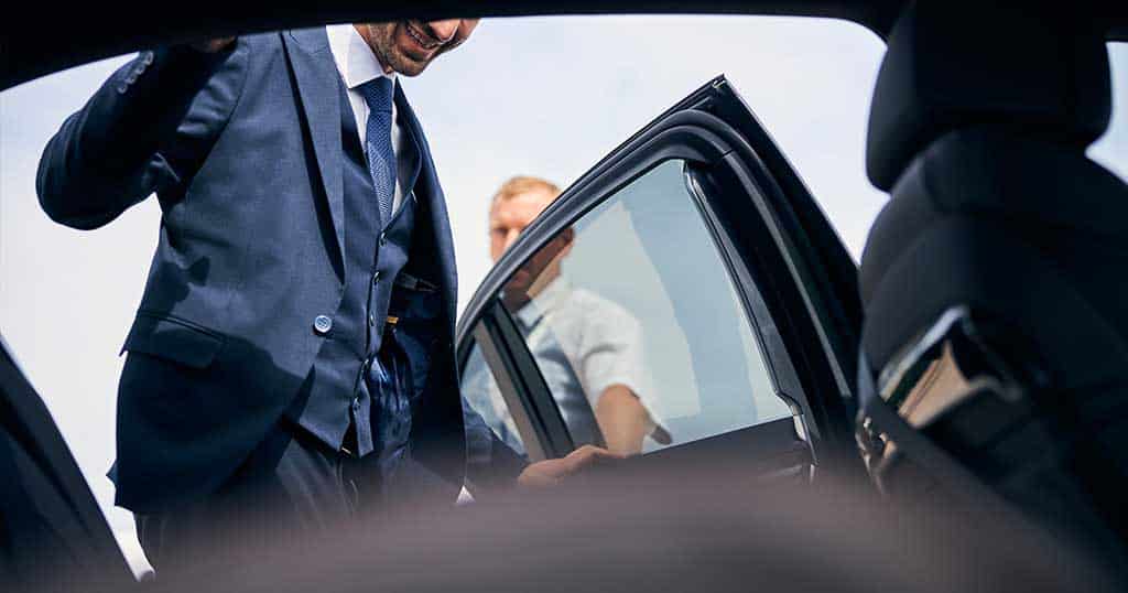 Executive protection agent opening the rear door of a black sedan