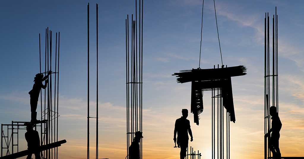 Construction crew silhouetted against a sunset sky on a rebar deck