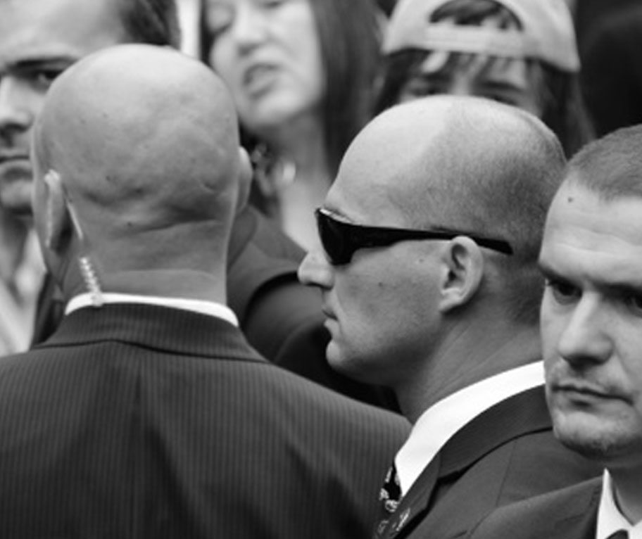 Close protection detail in suits coordinating in a public crowd