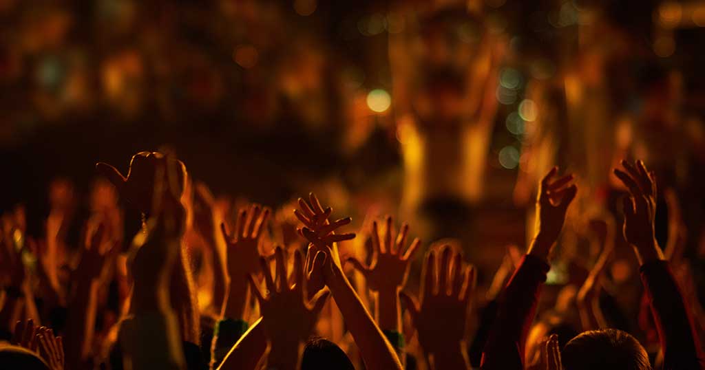 Hands raised at a worship gathering lit by warm stage lights